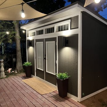 A modern, well-lit shed with double doors, potted plants, and outdoor lighting, showcasing Cypress Southern Homes' design in Tomball.